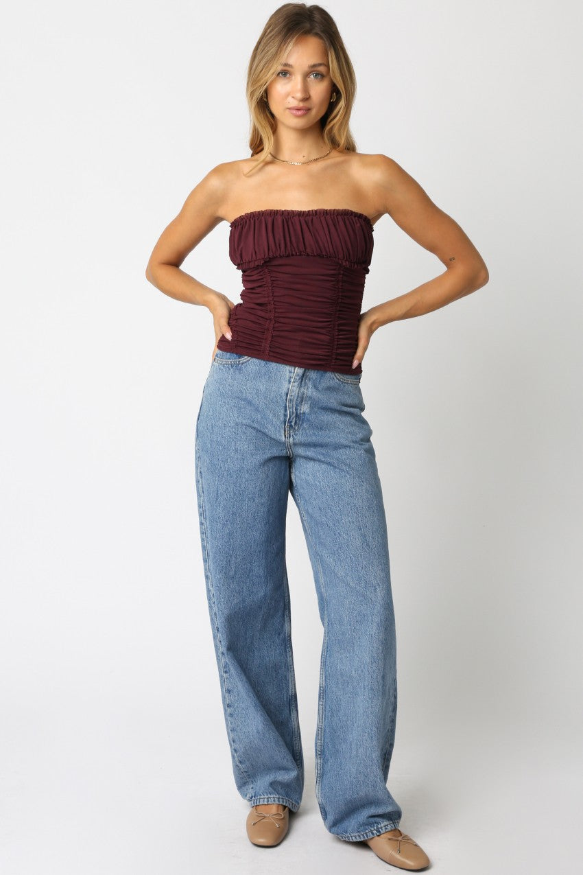 Woman wearing a strapless burgundy top and blue jeans on a white background