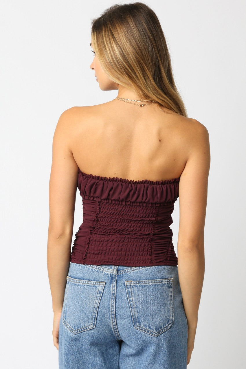 Woman wearing a strapless burgundy top and blue jeans on a white background