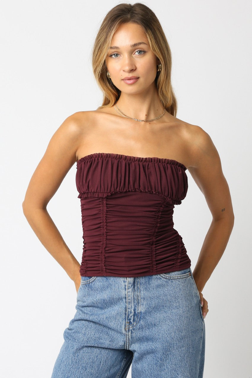 Woman wearing a burgundy strapless top and blue jeans on a white background